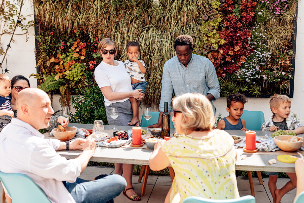 family, friends, adults, and kids having fun sitting or standing around the table on a sunny summer day.