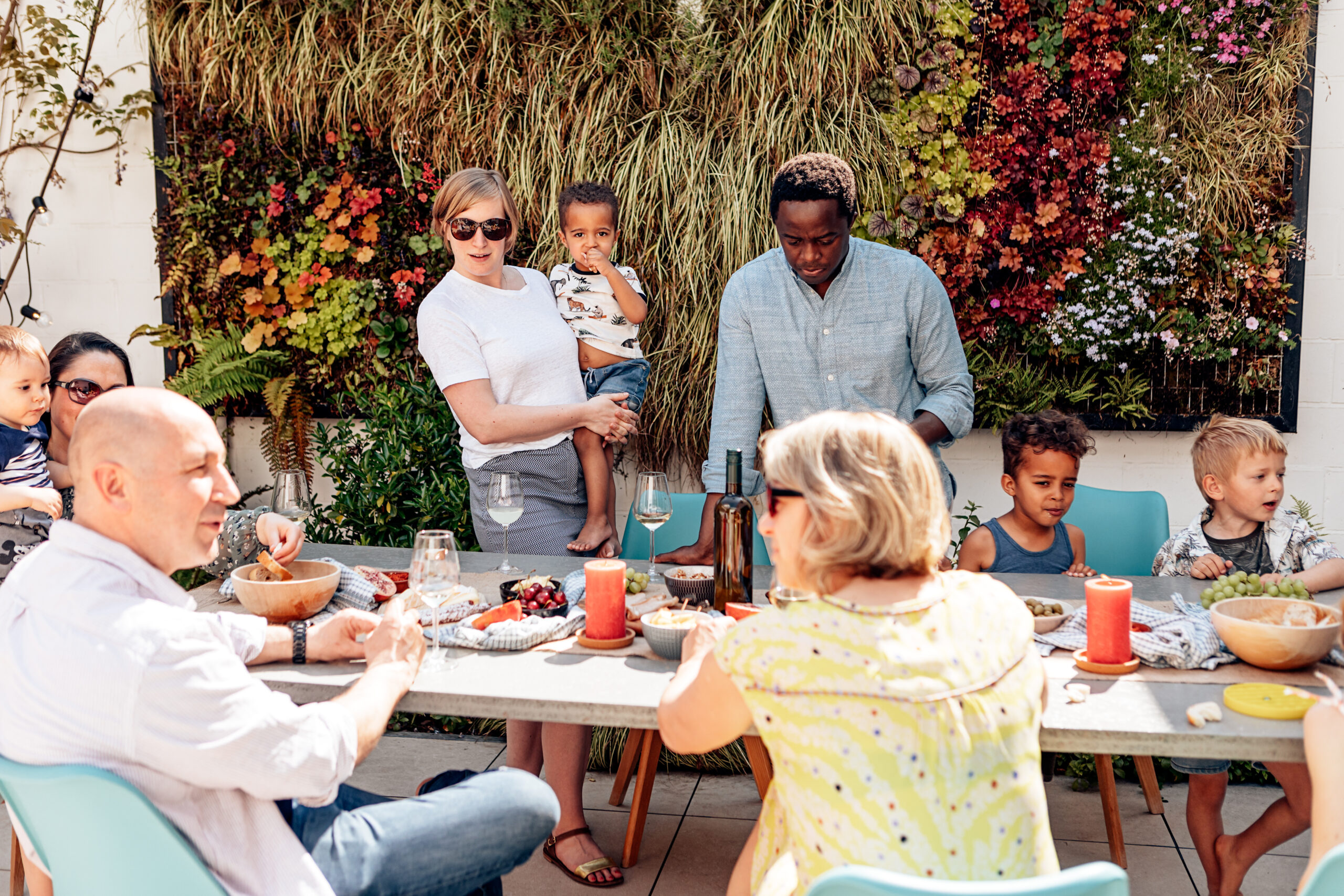 family, friends, adults, and kids having fun sitting or standing around the table on a sunny summer day.