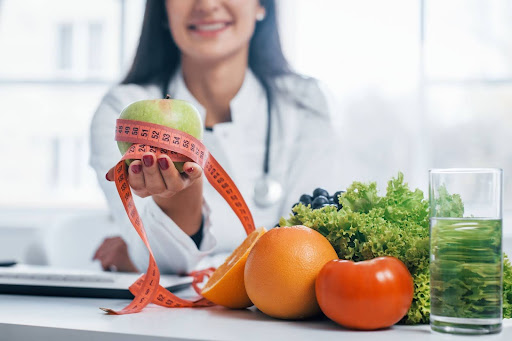 Doctor holds out a measuring tape next to vegetables.