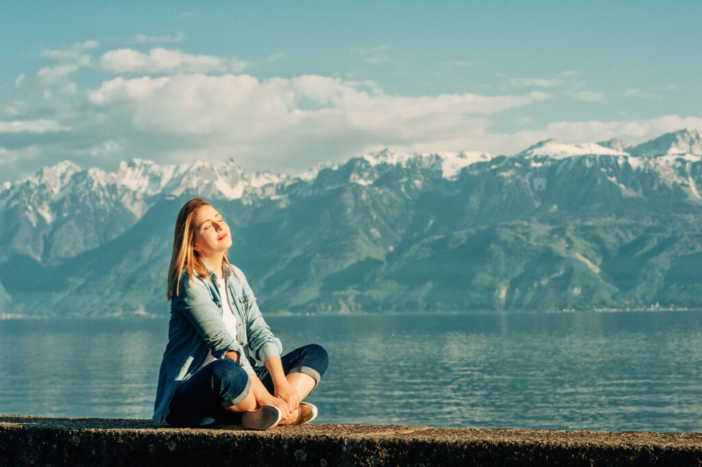 Outdoor portrait of happy young woman relaxing by the lake on a nice sunny day, peacful and harmonious mood