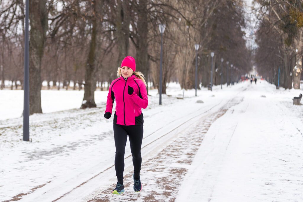 a woman running in the snow wearing a pink jacket and beanie