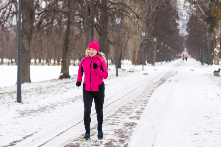 a woman running in the snow wearing a pink jacket and beanie